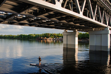 beautiful view on man floating under the bridge on sup board