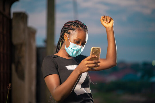 image of african lady in face mask, holding smart phone 