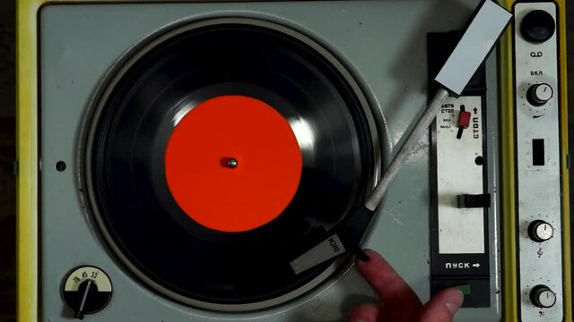Finger puts needle on vinyl record that is spinning on retro turntable