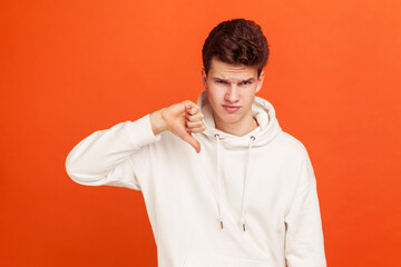 I don't like this. Young man in casual style hoodie showing thumb down sign with disgust on his...