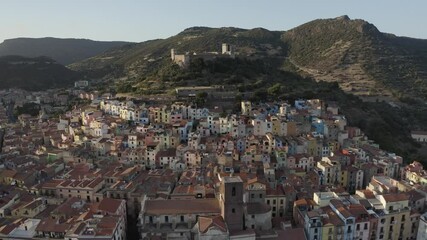 City view for colored houses below high green hill with a medieval castle on the top .Aerial shot during sunset and green mountains in the background