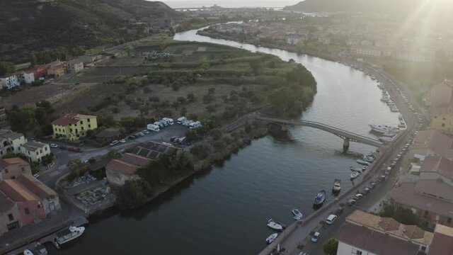 Static aerial shot for a curvy canal of the Temo River of Sardinia with no traffic and parked boats and river bridge during sunset.