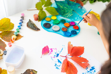little girl colors autumn leaves at home