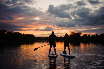 romantic view on man and woman on sup boards floating on river