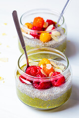 Green matcha tea chia seeds pudding with raspberries in a glass jar, white background.