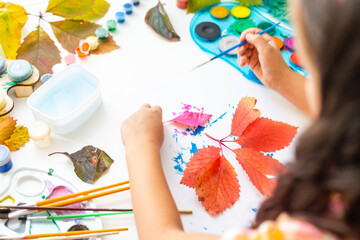 Obraz na płótnie Canvas little girl paints leaves with brush at home, autumn art.