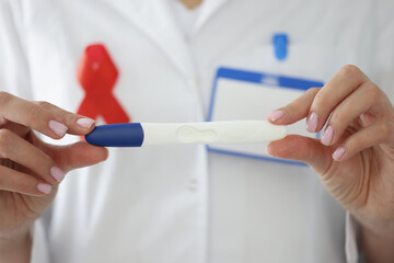 Doctor's hands with red ribbon on his chest hold pregnancy test closeup. Birth of healthy child from hiv positive mother concept.