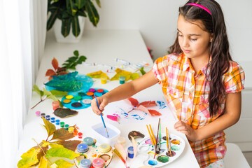 Little girl painting on autumn yellow leaves with gouache, kids arts, children creativity, autumn art.