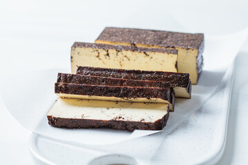 Sliced smoked tofu on white board, white background. Vegan food concept.