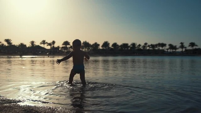 Adorable child walking in water on beach. Cute boy taking sand at seaside.