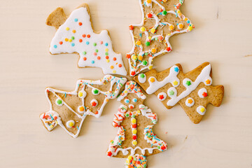 Five herringbone gingerbread cookies, differently decorated with glaze and sprinkles, set against a white painted wood texture.