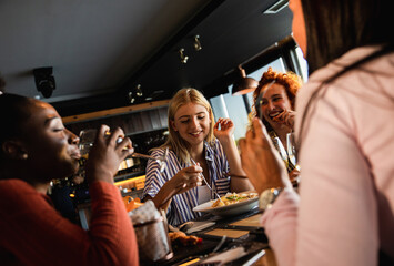 Group of young female friends having fun in restaurant, talking and laughing while dining at table.
