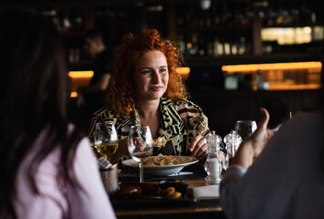 Group of young female friends having fun in restaurant, talking and laughing while dining at table.