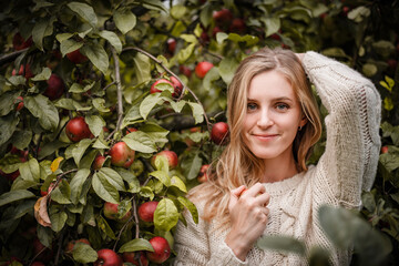 Blonde woman looking into camera holding an apple and wearing cozy sweater
