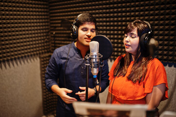 Young asian duet singers with microphone recording song in record music studio.