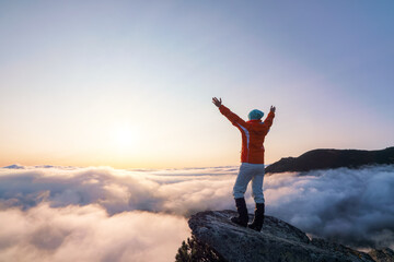 Successful sporty girl is standing at the edge of the precipice. Mountains landscape in the foggy morning. Sunrise. Autumn.