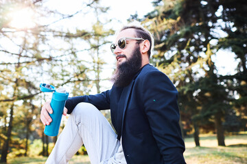 Bearded man drinking coffee in the woods after work