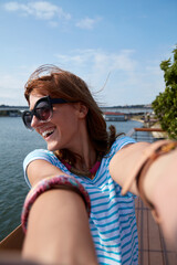 Young woman taking selfie outdoors near the river in city environment.