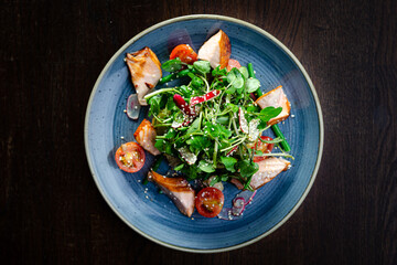 Kiln roast salmon salad with watercress, cherry tomatoes, radishes and sesame seeds on a blue plate...