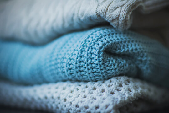Three warm knitted sweaters with patterns, one of which is blue, are neatly stacked. Warm clothes prepared for cold times. Winter and autumn.