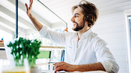 Obraz premium Handsome man with stubble sitting at home and working remote using laptop, greeting partner. Private house workplace