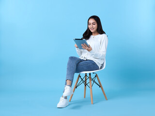 Young woman asian happy smiling in casual white cardigan with denim jeans.While her using tablet...