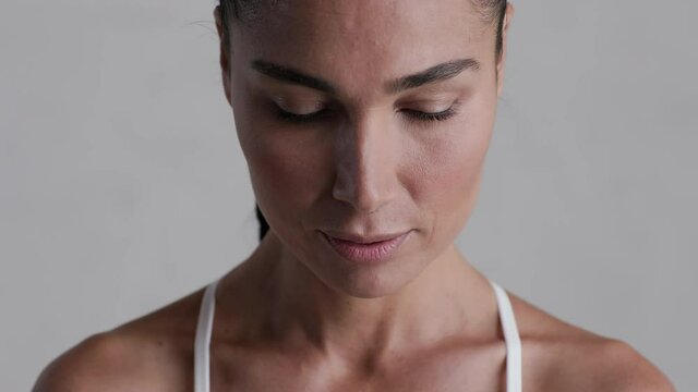 Portrait of determined latin girl breathing deeply isolated on grey background. Close up face of sporty woman preparing for a challenge on gray wall.