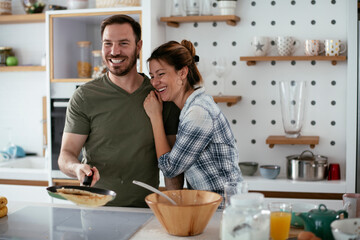 Young couple making pancakes at home. Loving couple having fun while cooking..