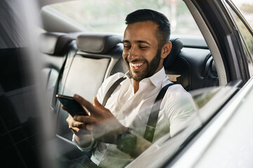 Bearded Indian Muslim businessman using smart phone shot through taxi car window