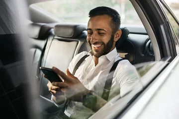 Papier Peint photo autocollant Abu Dhabi Bearded Indian Muslim businessman using smart phone shot through taxi car window