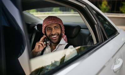 Arabic Muslim businessman looking out car window on mobile phone wearing Keffiyeh
