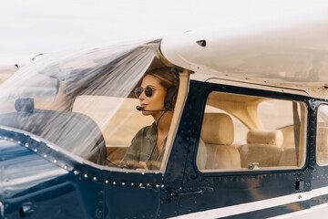 Woman pilot in airplane cabin, wearing headset and sunglasses. - obrazy, fototapety, plakaty