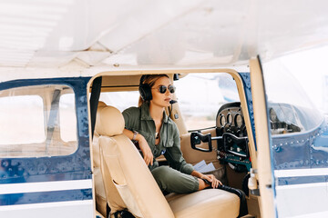 Woman pilot in private plane cockpit, wearing headset and sunglasses. - obrazy, fototapety, plakaty