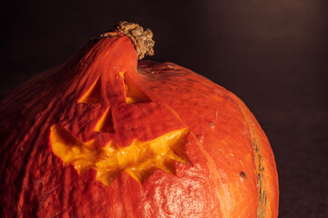 Hokkaido pumpkin with engraved scary face on dark table, useful for Helloween greeting card or social media