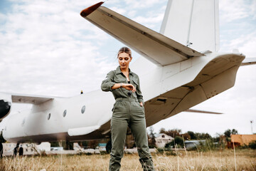Woman pilot wearing overall, standing in front of an airplane, looking at her watch.