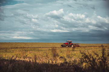 Fototapeta premium Tractor plowing the fields in the countryside. Agricultural tractor plowing the field. Red Tractor with plow.