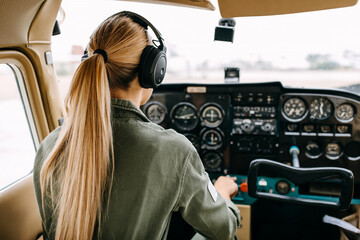 Back view over woman pilot flying an airplane, wearing headset. - Powered by Adobe