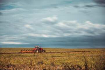 Fototapeta premium Tractor plowing the fields in the countryside. Agricultural tractor plowing the field. Red Tractor with plow.