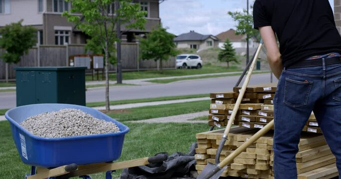 Young man shovels stones into wheel barrow - wide shot - slow motion