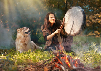 Shaman woman drumming in the sunny forest with an Alaskan Malamute dog