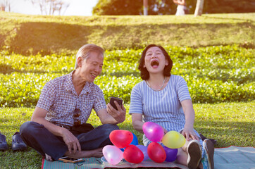 Fototapeta premium Happy senior asian couple looking at mobile phone feeling funny and laughing in the park