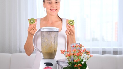 happy young woman preparing delicious nutritious smoothie in kiwi blender