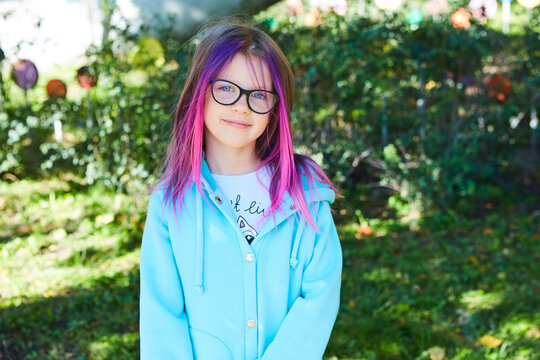 Beautiful portrait of a girl 8 years old with pink hair in the garden in summer.
