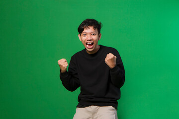 Young asian man on isolated green background. very happy and excited doing winner gesture with arms raised, smiling and screaming for success. Celebration concept.