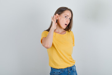 Young woman in t-shirt, shorts trying to hear secret and looking focused , front view.