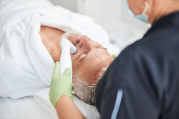 Obraz na płótnie Canvas Elderly man going through skin rejuvenation procedure at spa