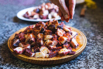 Portion of octopus cut in a wooden plate with the addition of paprika.