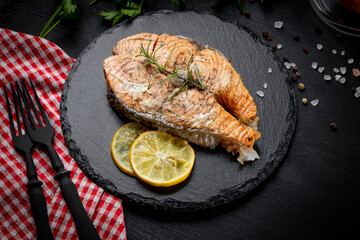 Baked salmon steak on a black slate plate and black background, close up