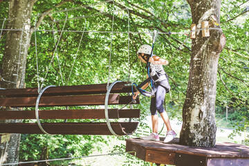 Little girl with safety equipment at the forest adventure park, amusement center for children outdoor