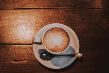 Taza de café con leche en un plato blanco sobre una mesa de madera con una cuchara de plata 